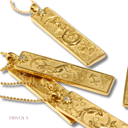 Gold-toned rectangular pendant necklaces with engraved zodiac and celestial motifs, shown on a white background with one necklace partially draped over another. The brand name FRIVOLA appears in the lower left.
